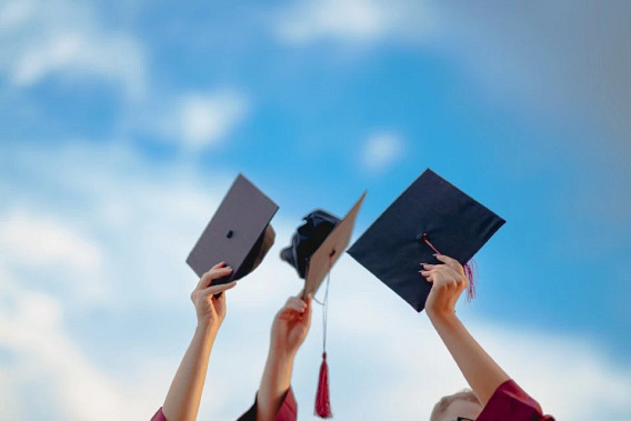 Three graduation caps held in the air by three college students wearing red gowns